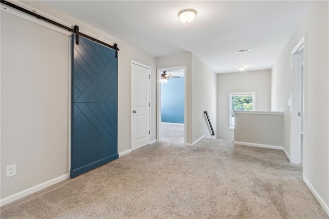 unfurnished room with light carpet, a barn door, and ceiling fan