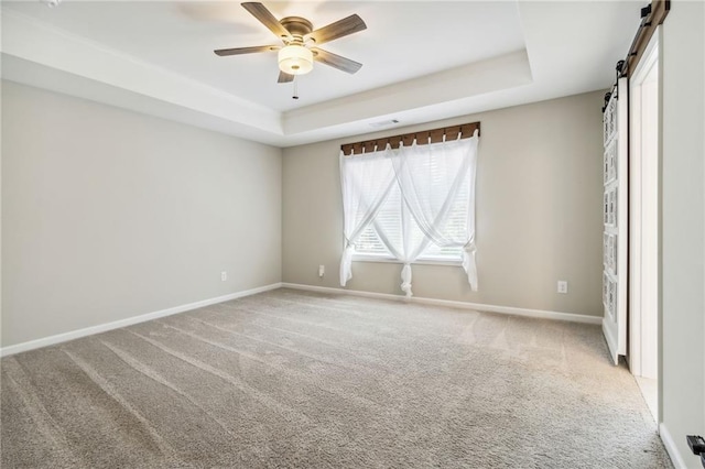 carpeted empty room featuring ceiling fan, a barn door, and a tray ceiling