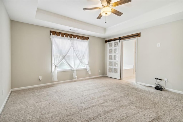 empty room with carpet, ceiling fan, a barn door, and a tray ceiling