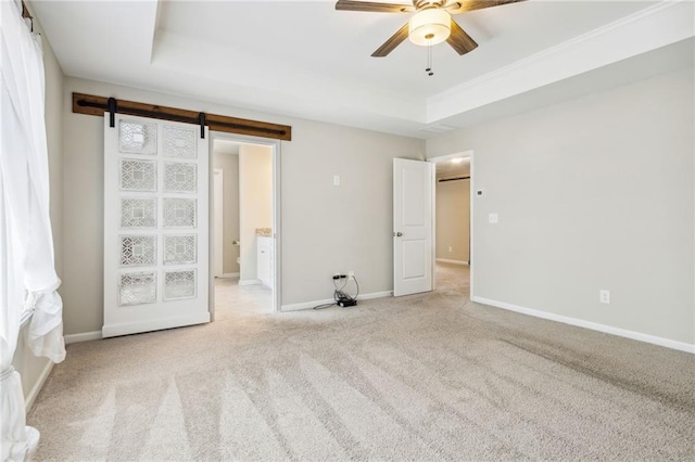 unfurnished bedroom with a tray ceiling, a barn door, ceiling fan, and light carpet