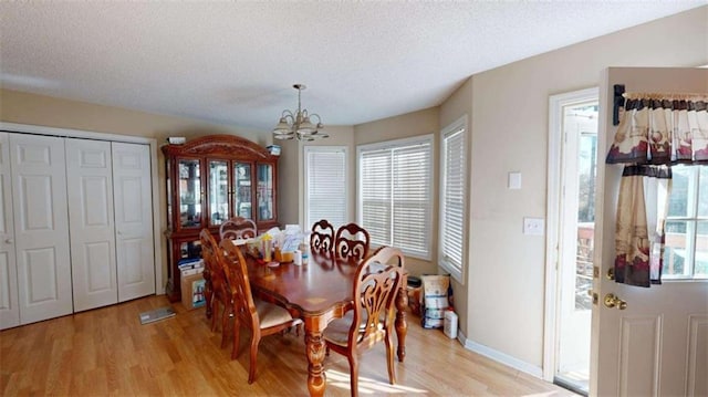 dining room with light hardwood / wood-style floors, a textured ceiling, and a notable chandelier