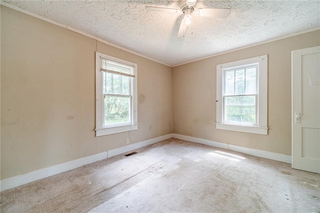 carpeted empty room with visible vents, ornamental molding, baseboards, a textured ceiling, and a ceiling fan