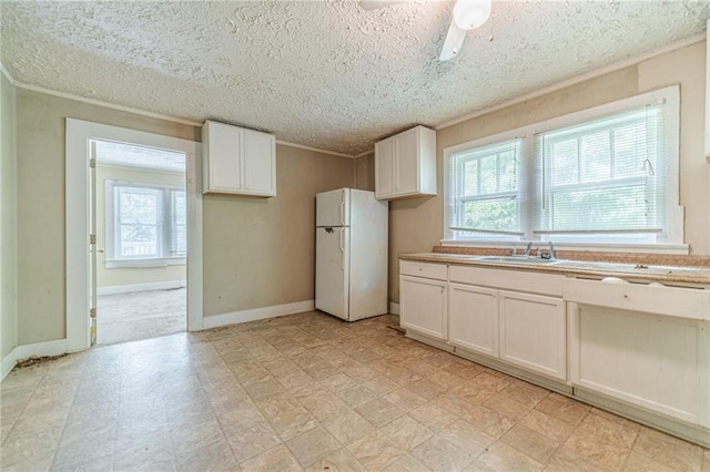 kitchen featuring a healthy amount of sunlight, light floors, ornamental molding, and freestanding refrigerator