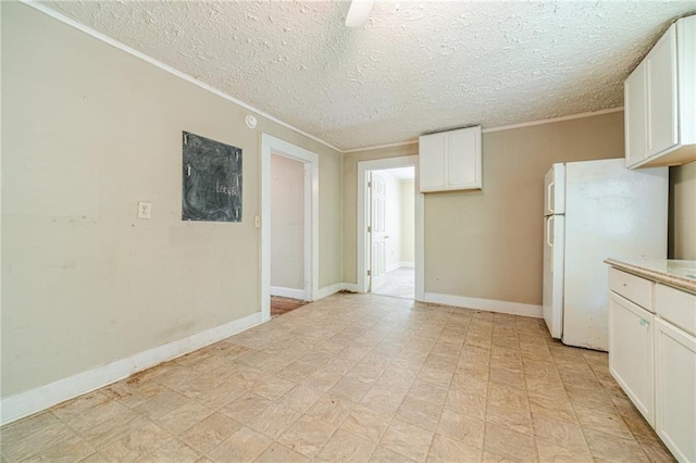 kitchen with white cabinets, light countertops, a textured ceiling, freestanding refrigerator, and ornamental molding