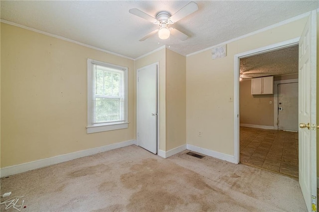 unfurnished bedroom featuring a textured ceiling, visible vents, baseboards, ornamental molding, and carpet flooring