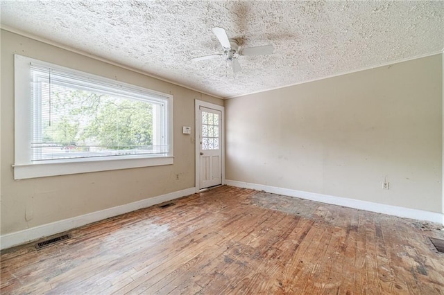 empty room with wood-type flooring, a ceiling fan, a textured ceiling, and visible vents