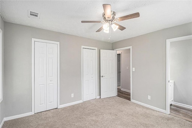 unfurnished bedroom featuring two closets, visible vents, baseboards, and carpet floors