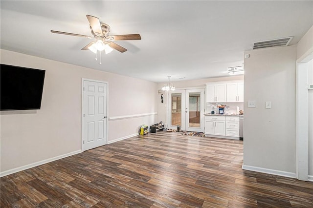 unfurnished living room featuring ceiling fan with notable chandelier, baseboards, visible vents, and dark wood finished floors