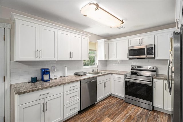 kitchen with dark wood-style flooring, light stone counters, a sink, white cabinets, and appliances with stainless steel finishes