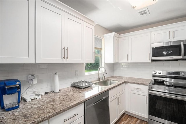 kitchen featuring a sink, stainless steel appliances, light stone counters, visible vents, and white cabinetry