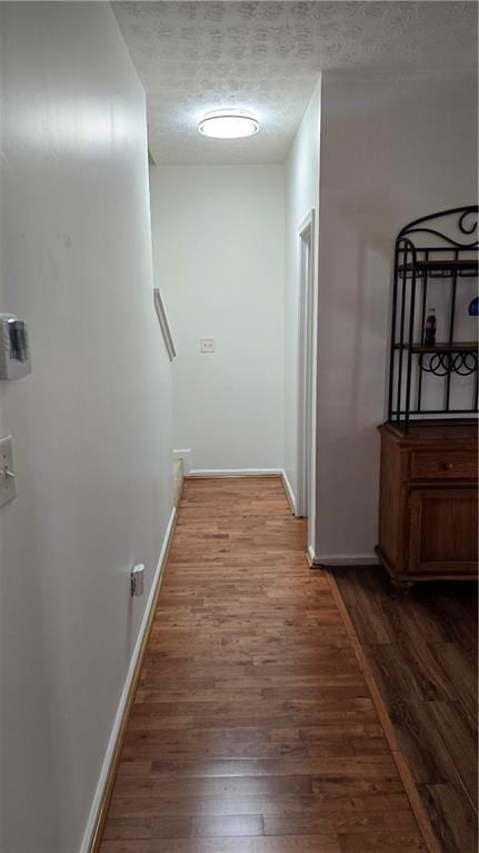 hall featuring a textured ceiling, baseboards, and wood finished floors