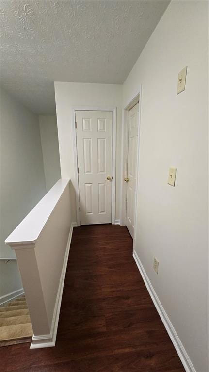 corridor with an upstairs landing, wood finished floors, baseboards, and a textured ceiling