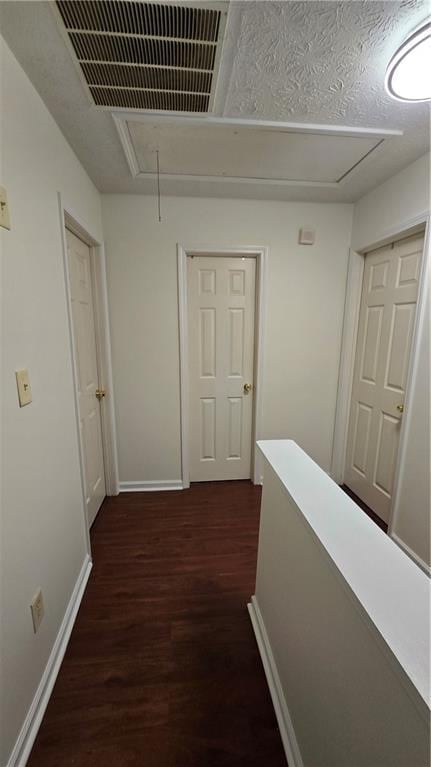 corridor featuring visible vents, baseboards, attic access, a textured ceiling, and dark wood-style flooring