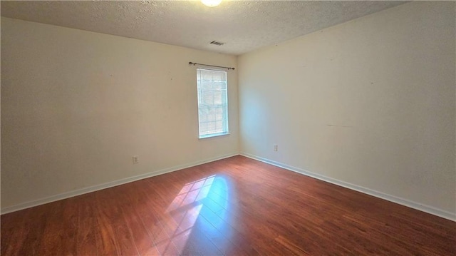 spare room with visible vents, baseboards, dark wood-type flooring, and a textured ceiling