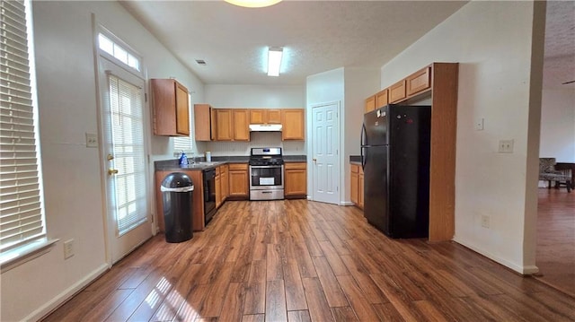 kitchen with dark countertops, visible vents, under cabinet range hood, wood finished floors, and black appliances