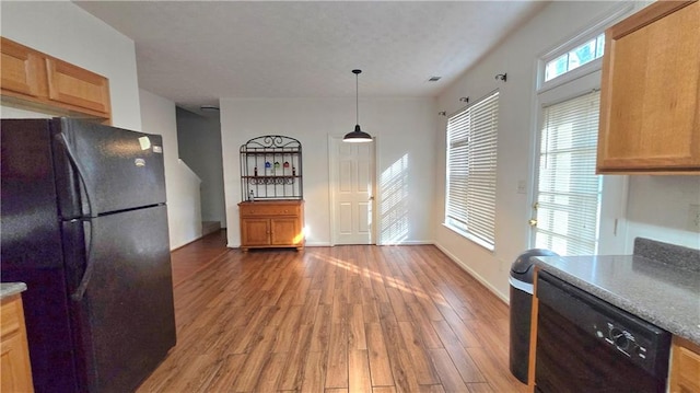 kitchen with light wood-type flooring, brown cabinets, black appliances, baseboards, and hanging light fixtures