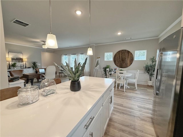 kitchen featuring crown molding, stainless steel refrigerator, white cabinetry, light hardwood / wood-style floors, and decorative light fixtures