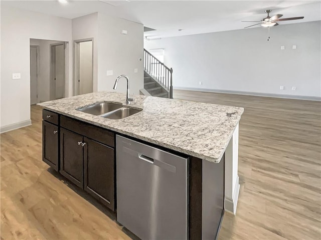 kitchen featuring light wood finished floors, baseboards, dishwasher, an island with sink, and a sink