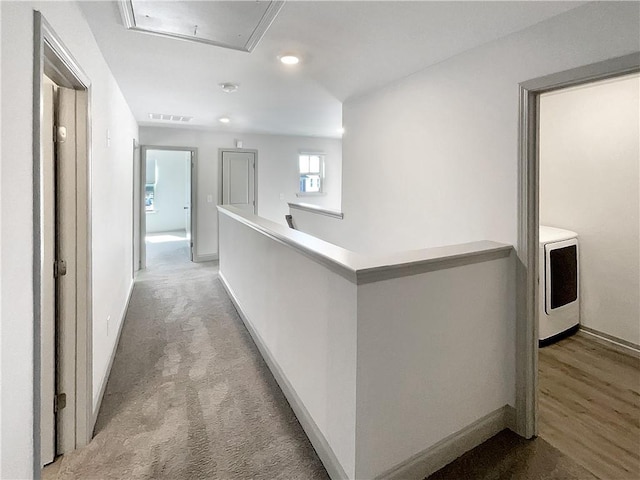 corridor with visible vents, washer / dryer, attic access, an upstairs landing, and light colored carpet