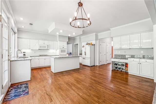 kitchen featuring hardwood / wood-style floors, a center island, white cabinets, white appliances, and hanging light fixtures