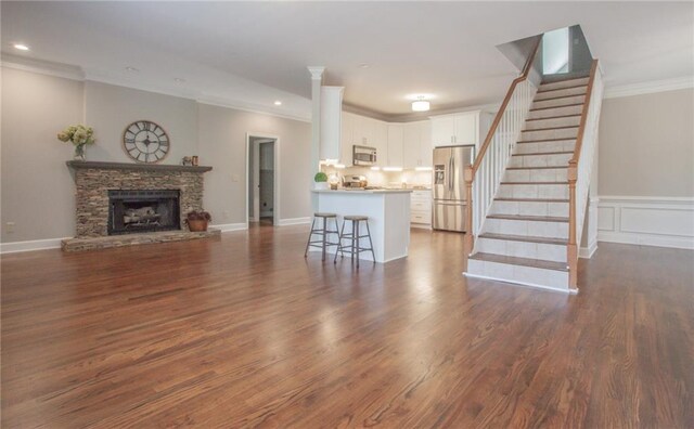 living room with dark hardwood / wood-style floors, ornamental molding, and a stone fireplace