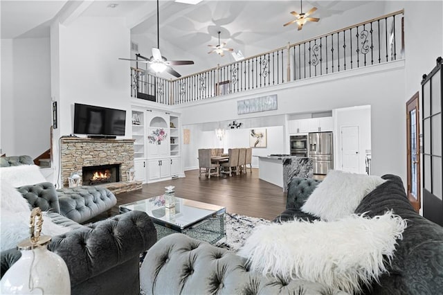 living room featuring dark hardwood / wood-style floors, beam ceiling, a stone fireplace, and high vaulted ceiling