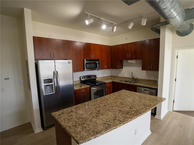 kitchen with a kitchen island, light wood-style flooring, a sink, appliances with stainless steel finishes, and backsplash