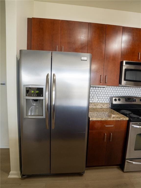 kitchen featuring backsplash, appliances with stainless steel finishes, light wood-style flooring, and light stone countertops