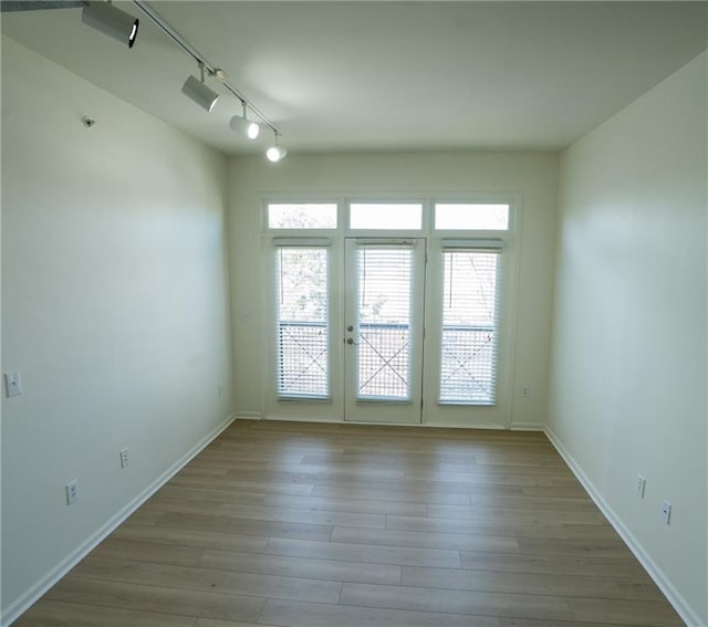 spare room featuring rail lighting, wood finished floors, baseboards, and a wealth of natural light