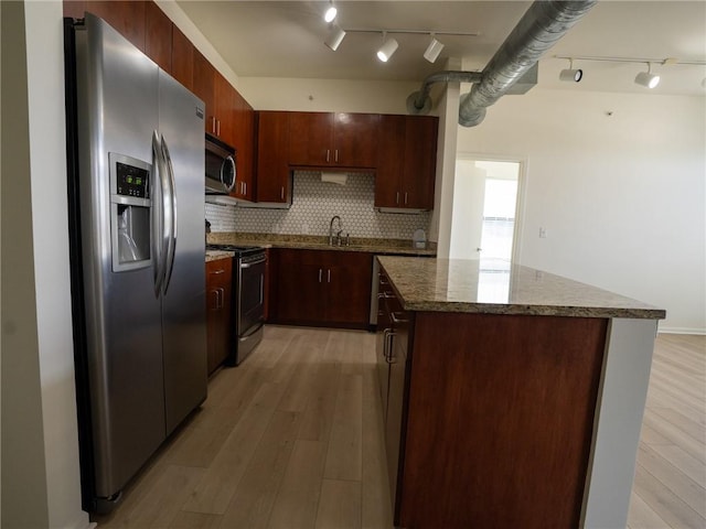 kitchen with a kitchen island, light wood-type flooring, dark stone counters, appliances with stainless steel finishes, and tasteful backsplash