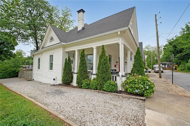 view of side of property with a porch, fence, a chimney, and a shingled roof
