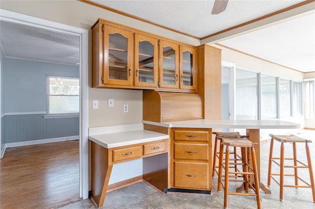 kitchen featuring built in desk, light hardwood / wood-style floors, a textured ceiling, a kitchen bar, and ornamental molding