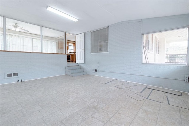 unfurnished room featuring vaulted ceiling, ceiling fan, and brick wall