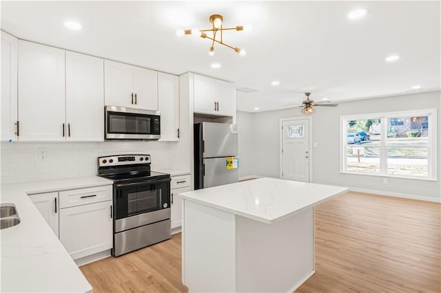 kitchen featuring stainless steel appliances, a kitchen island, backsplash, white cabinets, and ceiling fan with notable chandelier