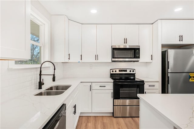 kitchen featuring white cabinets, sink, decorative backsplash, light hardwood / wood-style floors, and stainless steel appliances