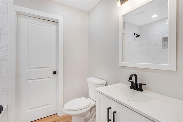 bathroom featuring hardwood / wood-style flooring, vanity, toilet, and tiled shower