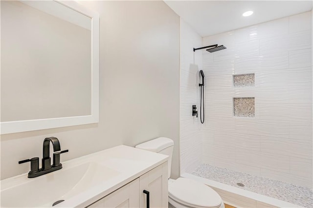 bathroom featuring a tile shower, vanity, and toilet