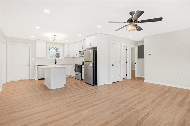 kitchen with white cabinets, ceiling fan with notable chandelier, light hardwood / wood-style floors, appliances with stainless steel finishes, and a kitchen island