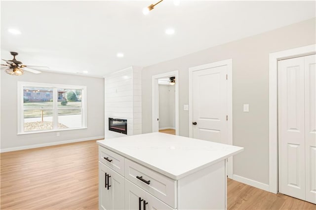 kitchen with a center island, white cabinets, ceiling fan, light wood-type flooring, and a large fireplace