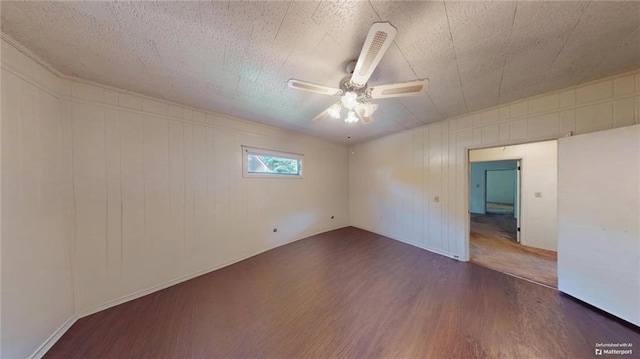 unfurnished room featuring a textured ceiling, wooden walls, ceiling fan, and dark wood-type flooring