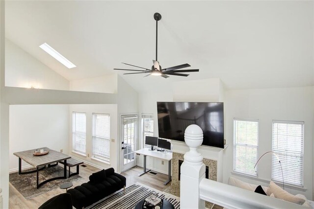 living room with a skylight, ceiling fan, high vaulted ceiling, and light wood-type flooring