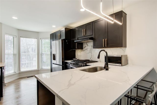 kitchen with stainless steel appliances, light stone counters, kitchen peninsula, a kitchen bar, and light wood-type flooring