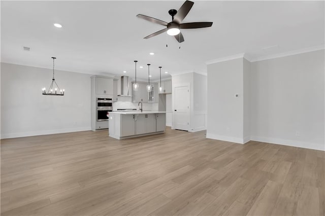 unfurnished living room featuring sink, ceiling fan with notable chandelier, light wood-type flooring, and ornamental molding