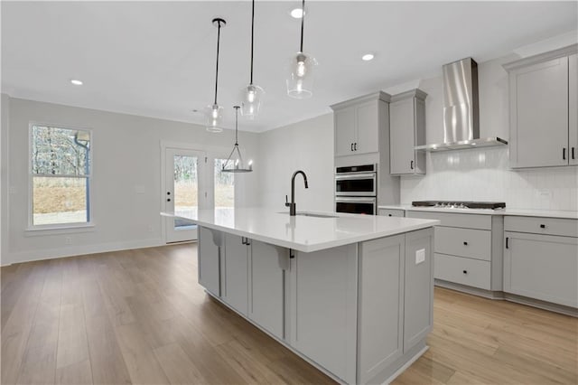 kitchen with wall chimney exhaust hood, pendant lighting, a center island with sink, gray cabinetry, and sink