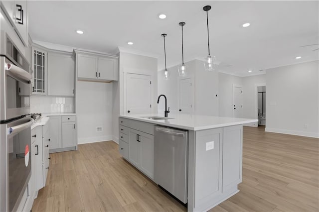 kitchen with appliances with stainless steel finishes, light wood-type flooring, sink, and a center island with sink