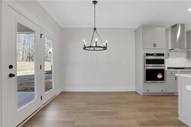 kitchen with an inviting chandelier, appliances with stainless steel finishes, light hardwood / wood-style flooring, wall chimney range hood, and decorative light fixtures