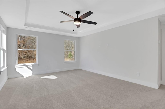 empty room featuring ceiling fan, light carpet, and a tray ceiling