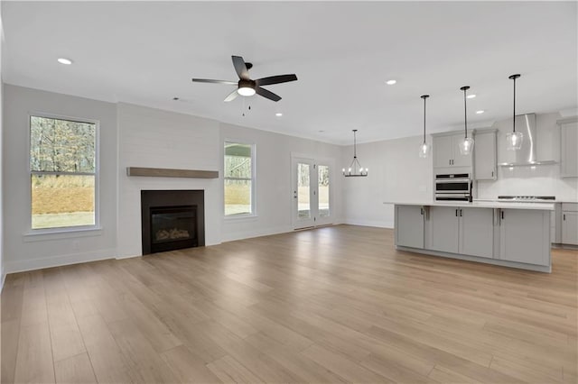 unfurnished living room featuring ceiling fan with notable chandelier, light hardwood / wood-style floors, a fireplace, and a wealth of natural light