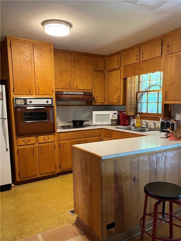 kitchen featuring kitchen peninsula, sink, white appliances, and a breakfast bar area