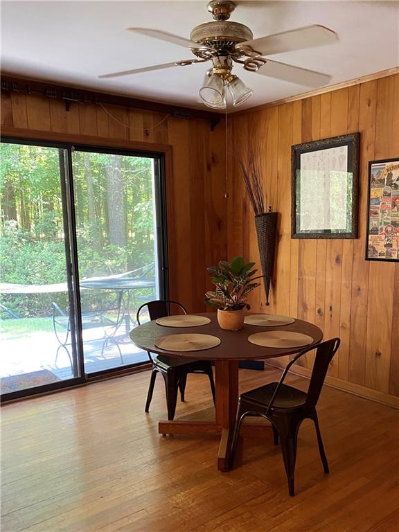 dining area featuring ceiling fan, wood walls, and hardwood / wood-style floors